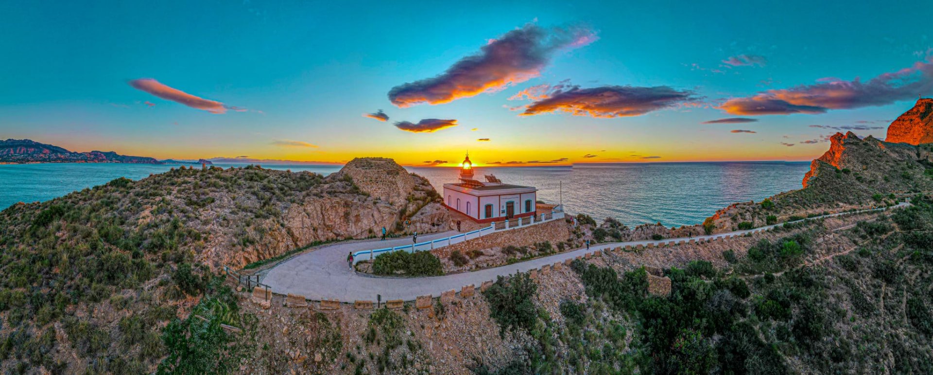 Faro del Albir lighthouse on a cliff at sunset with the Bay of Altea in the background