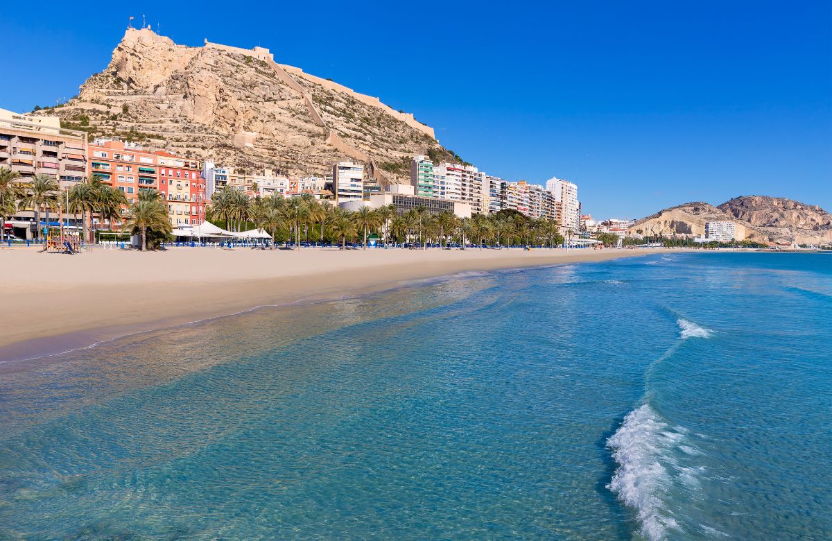 Postiguet beach in Alicante with calm turquoise water and Santa Bárbara castle in the background, perfect for families in October